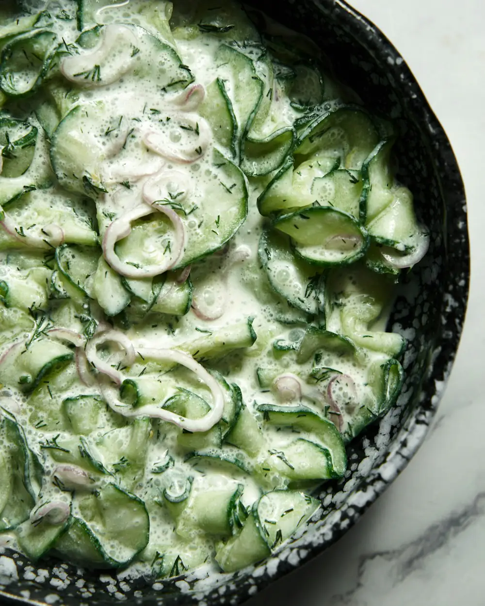 Geraspelte Gurke in Joghurt mit Dill, in einer dunklen Schale.