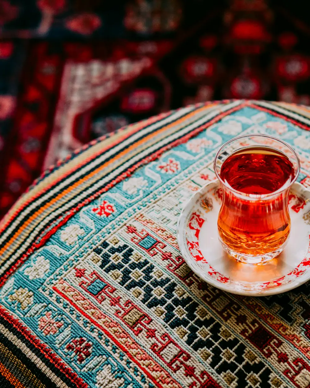 Ein schmales Teeglas mit dunklem Schwarztee auf einem gemusterten Textil.