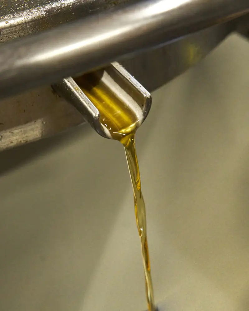 Goldenes Öl läuft in einem dünnen Strahl aus einem Metallauslauf.