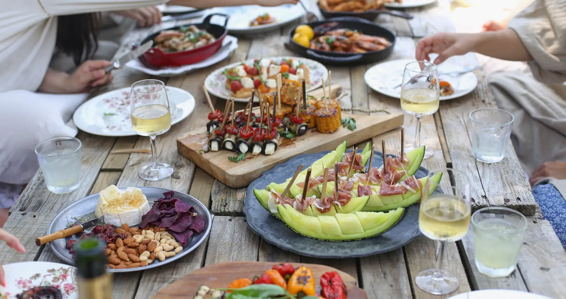 Eine Gruppe sitzt draußen an einer langen Tafel und teilt sich das Essen.